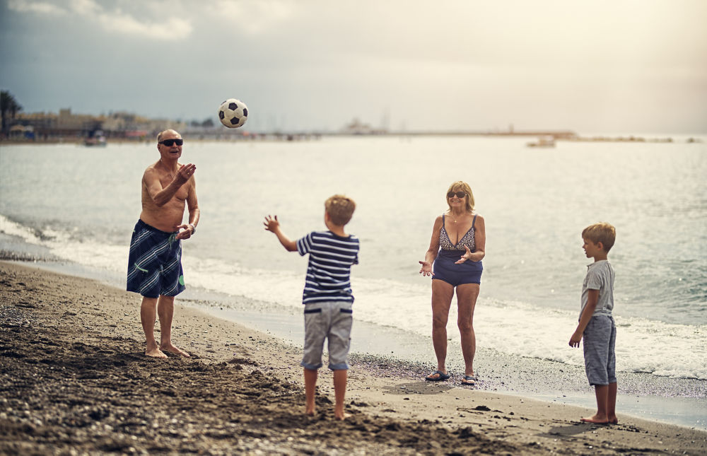 Niños pequeños jugando a la pelota con su abuela y su abuelo. Los niños tienen 7 años. Familia disfrutando de un día soleado de verano en la playa.