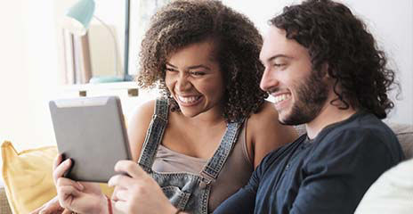 Pareja feliz usando una tableta digital en un sofá, en casa