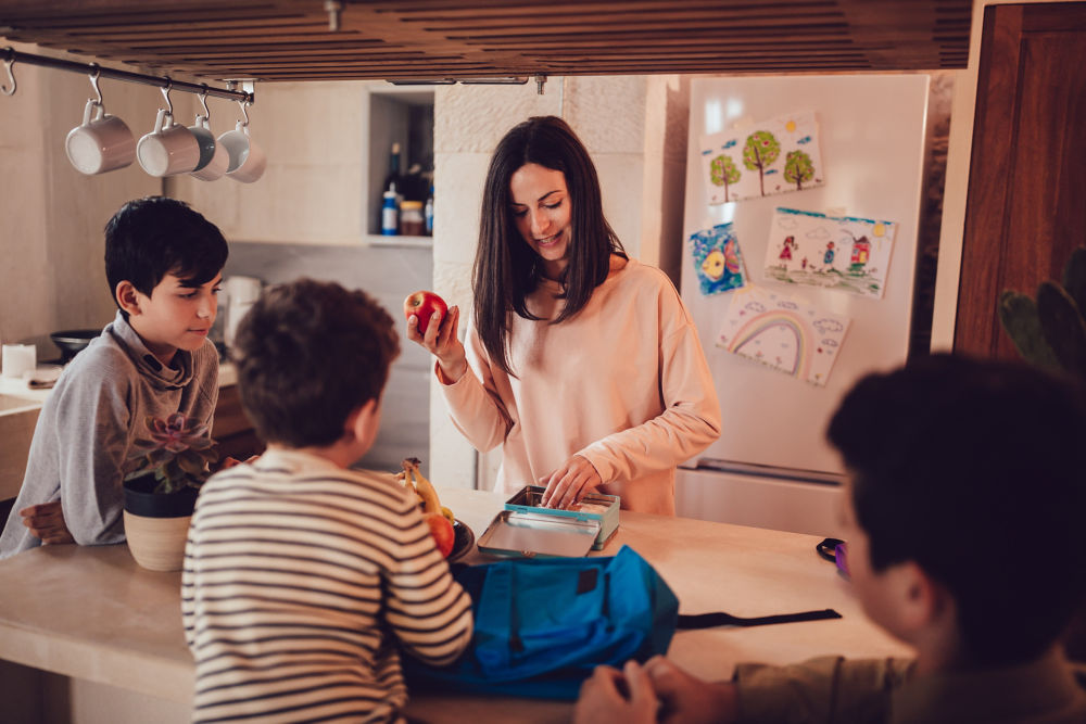 Madre preparando loncheras con comida saludable y refrigerios para los hijos antes de ir a la escuela