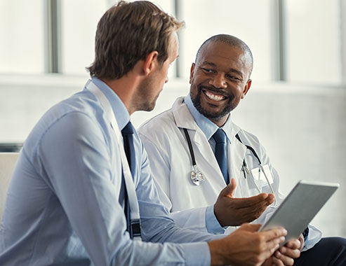 Two mature smiling doctors having discussion about patient diagnosis, holding digital tablet. Successful african surgeon discussing case after positive result. Representative pharmaceutical discussing with african happy doctor about new medicine.