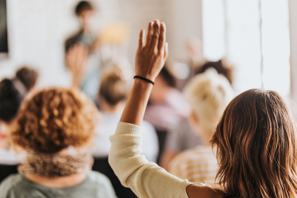 Rear view of casual businesswoman raising her arm to ask the question on education event in a board room.