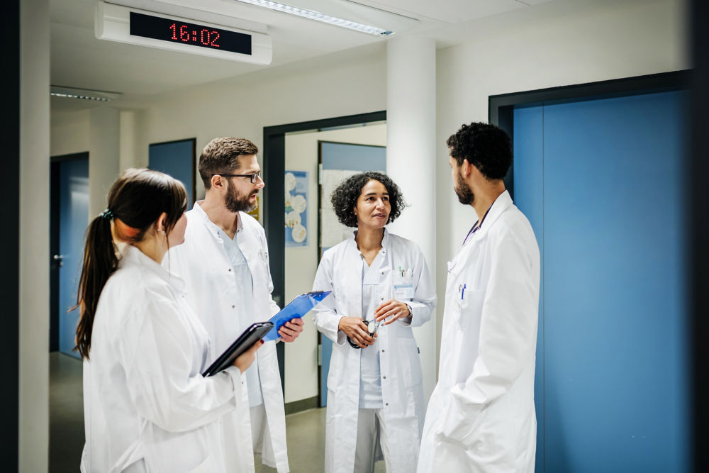 Un grupo de médicos clínicos con historias clínicas conversando en la sala del hospital.