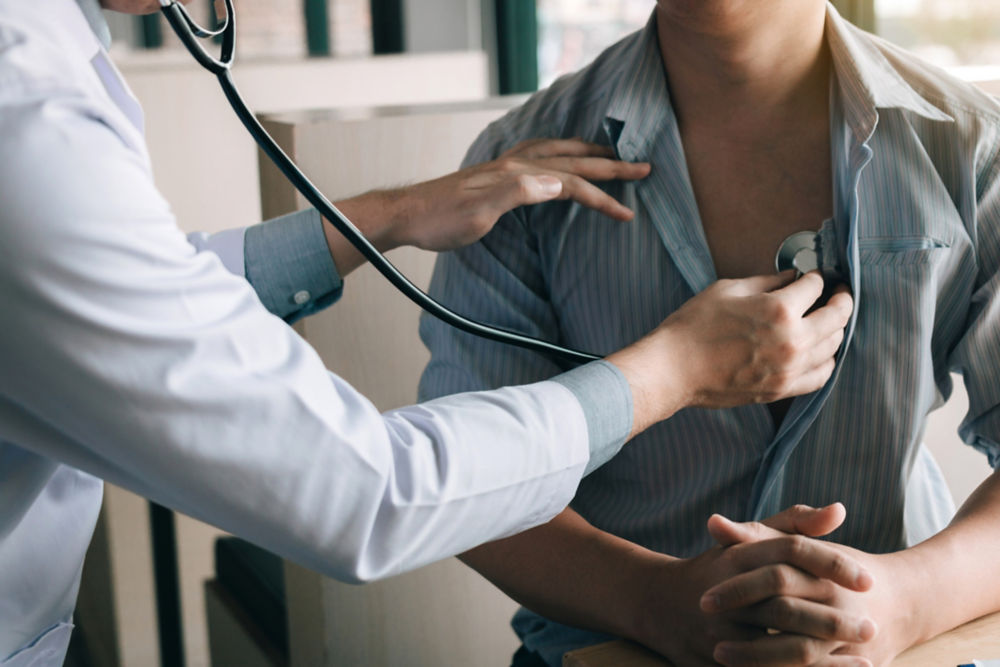 Médico asiático utilizando un estetoscopio para escuchar los latidos del corazón del paciente anciano.