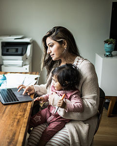 Mother multi-tasking with infant daughter in home office