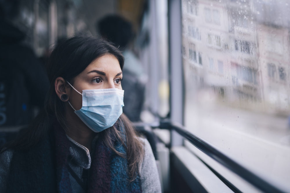 Mujer joven usando una mascarilla protectora sentada en el transporte por autobús en la ciudad.