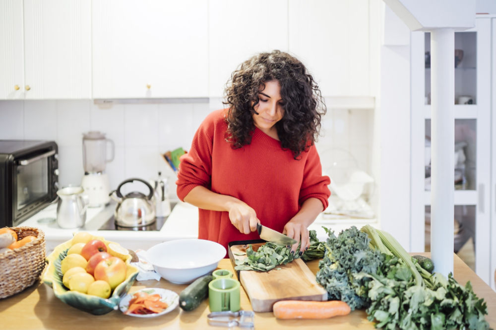 Mujer morena preparando una ensalada verde saludable.