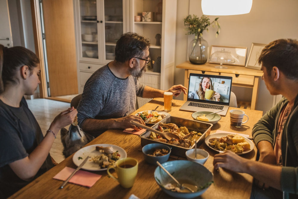 Family have diner during isolation period. Mother is not with them, they talking with her on laptop