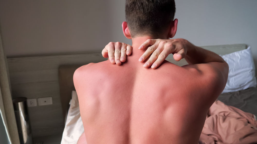 Hombre musculoso con la espalda desnuda masajeando el cuello y los hombros con las manos de pie en la cama en la habitación del hotel vista trasera cerrada