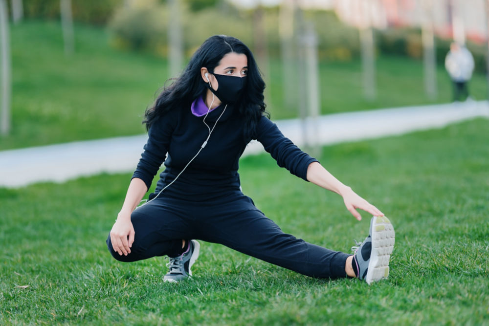 Mujer joven haciendo estiramientos sobre el césped de un parque público