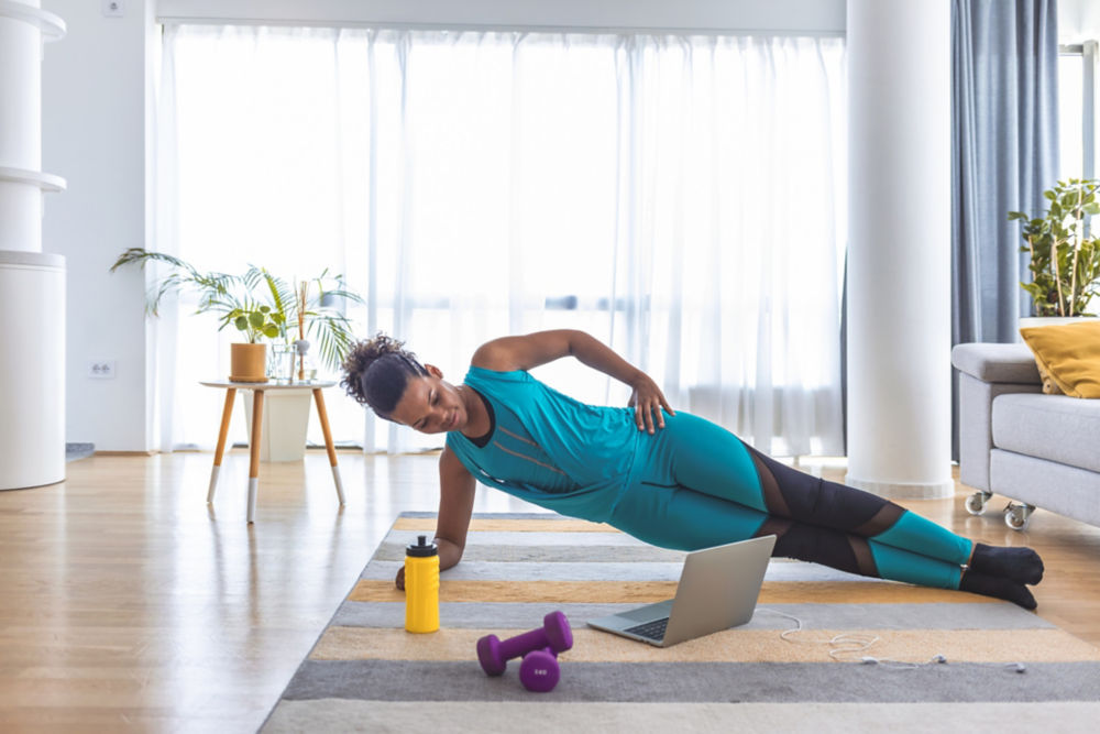 Beautiful woman doing fitness exercise at home while looking at laptop.