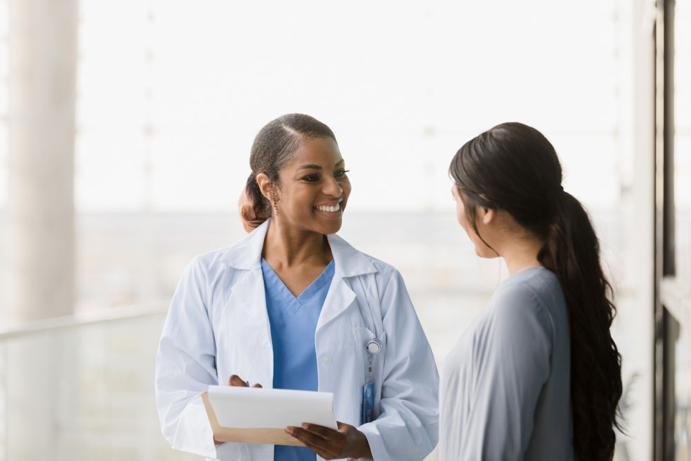 Standing in the hospital walkway, the mid adult female doctor and the unrecognizable young adult woman discuss the good test results.