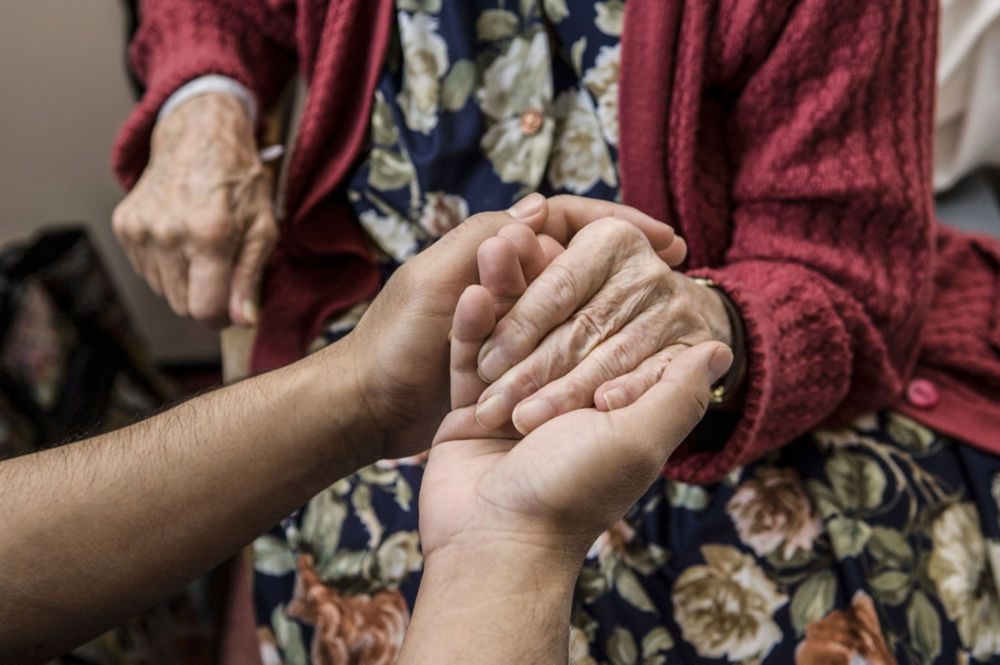 Enfermera tomada de la mano de un paciente anciano.