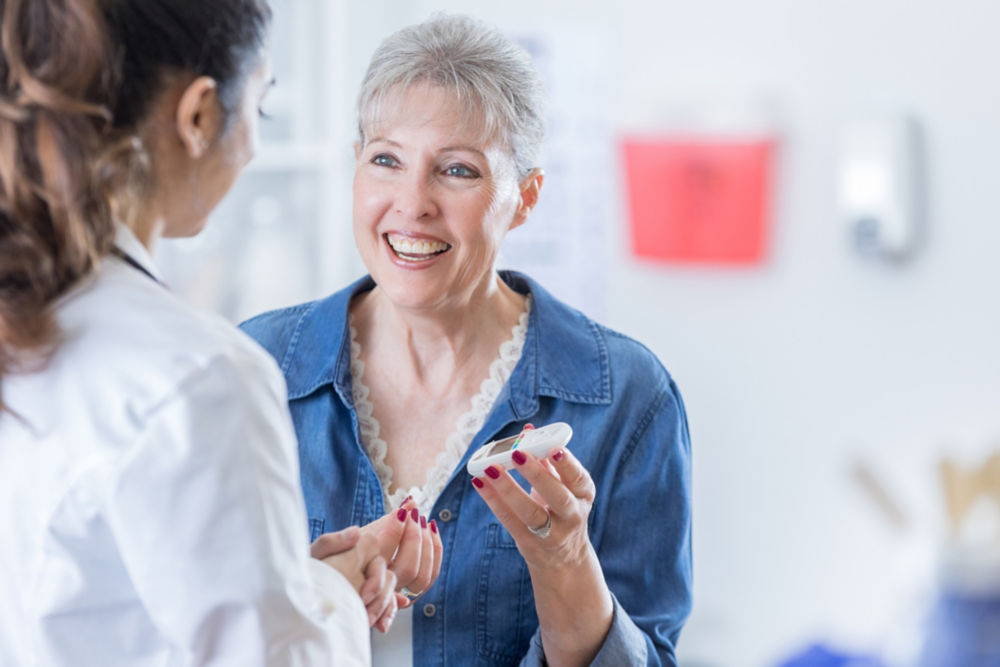 Smiling senior woman holds a glaucometer to check her blood sugar level. She is talking with her doctor.