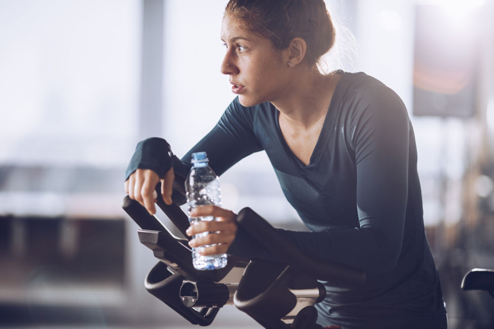 Deportista cansada tomándose un descanso para tomar agua durante la clase de ejercicio en un gimnasio.