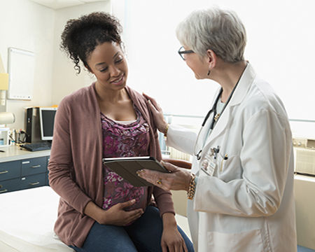 Gynecologist with digital tablet comforting pregnant patient