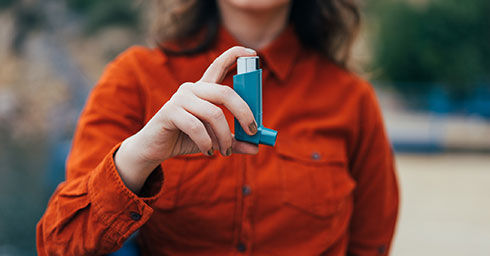 Young woman using an asthma inhaler outdoors