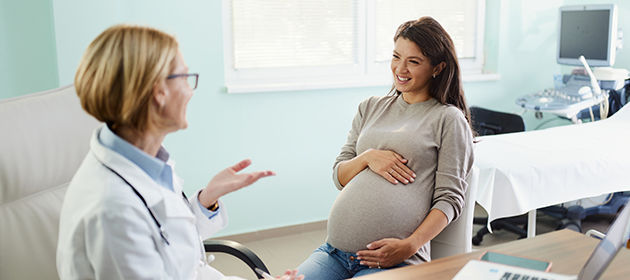 Mujer embarazada feliz hablando con su ginecóloga durante una visita al consultorio.