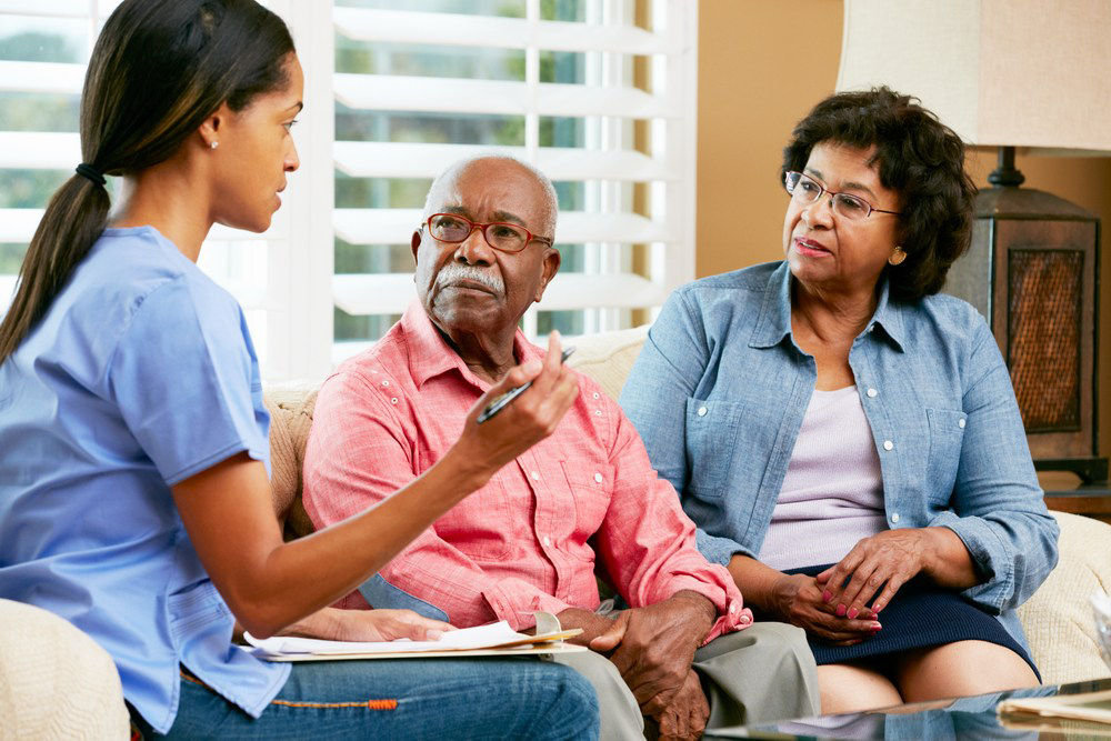 Older couple sitting on couch talking with a nurse.