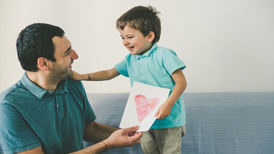 Father and son are next two each other. Son is giving heart drawing to his father.