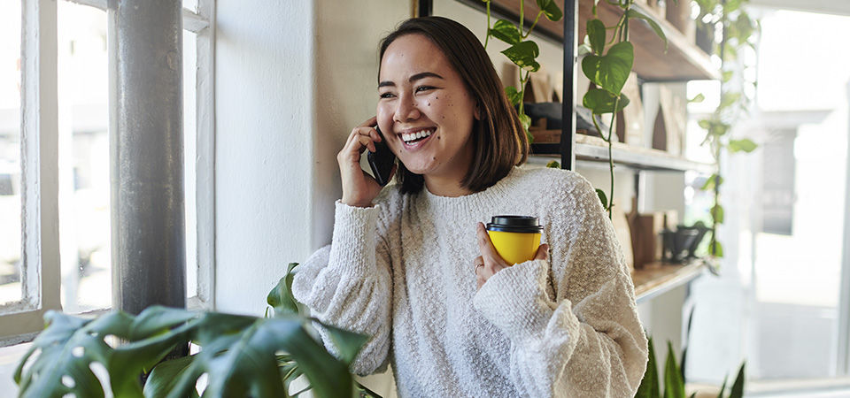 persona hablando por teléfono sosteniendo café y sonriendo