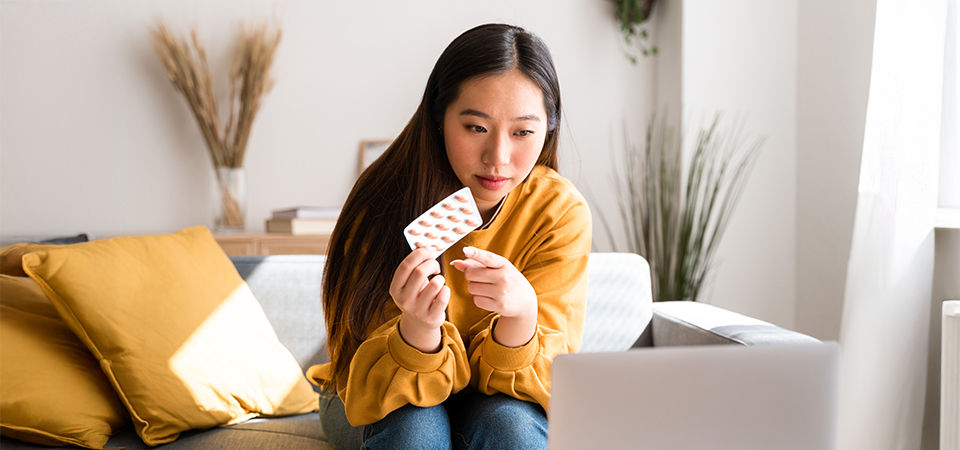 woman holding medicine and sitting at computer 