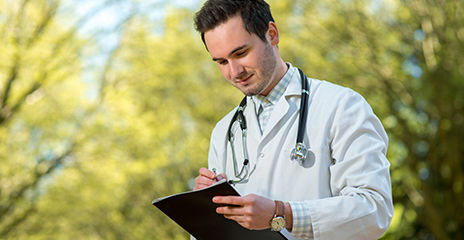 doctor writing and smiling outside with trees