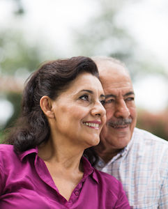 A happy senior latin couple looking away in a horizontal head and shoulders shot outdoors.