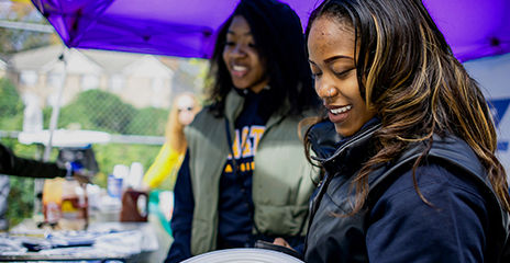 Two people outside at a neighborhood care event table and smiling