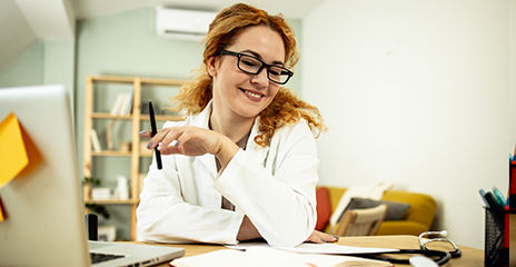 Healthcare professional holding pen with laptop and smiling