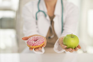 Doctor is holding a donut and an apple for diabetes awareness.