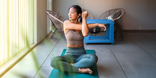  woman dressed in workout attire engrosses in yoga, gracefully stretching on a mat in her balcony space, with domestic tranquility as her backdrop.