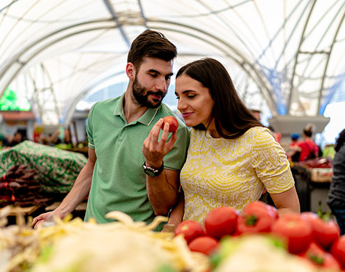 two people at a farmers market holding fruit