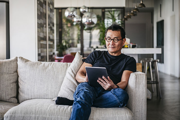 Chinese man in his 50s relaxing at home on sofa, casual clothes, reading ebook, surfing the internet