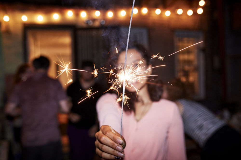Mujer de raza mixta sonriente sosteniendo una bengala ardiente en una fiesta en el patio trasero