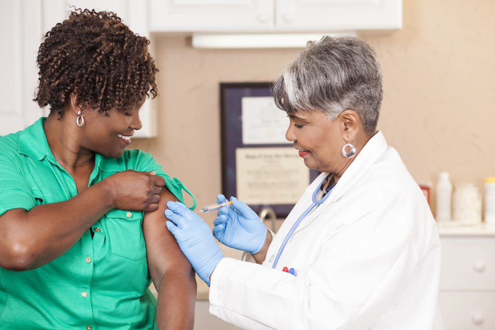 Senior adult doctor or nurse gives flu vaccine to African descent, mid-adult patient at a local medical clinic, hospital, or doctor's office.  NOTE:  This is a studio shot and not an actual medical clinic.