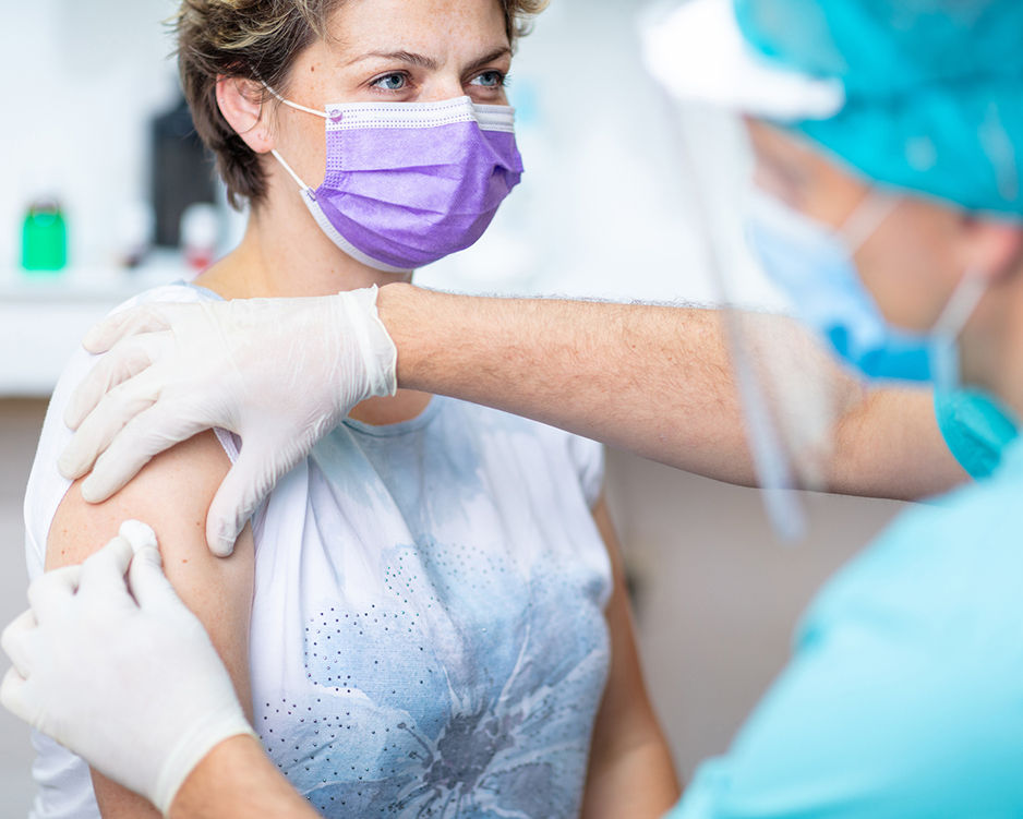 Female patient with protective face mask waiting for vaccination, doctor in surgical gloves disinfecting her arm