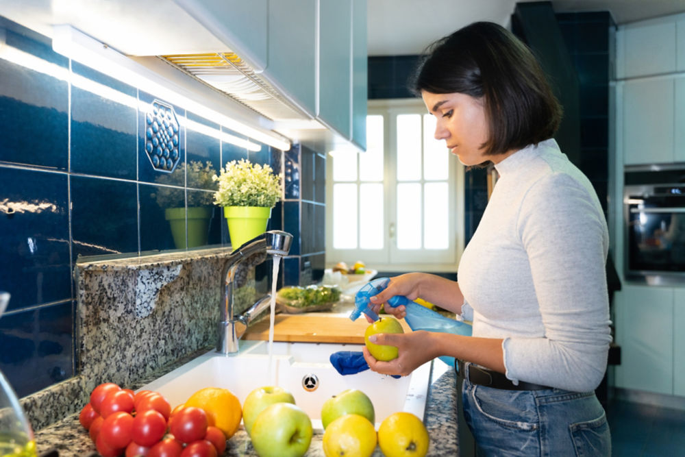 Mujer desinfectando comestibles en su cocina, para evitar el COVID-19. Ella lava toda la comida después de hacer las compras para prevenir enfermedades.