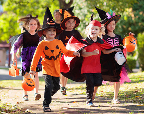 Child in Halloween costume. Mixed race Asian and Caucasian kids and parents trick or treat on street. Little boy and girl with pumpkin lantern and candy bucket. Baby in witch hat. Autumn holiday fun.