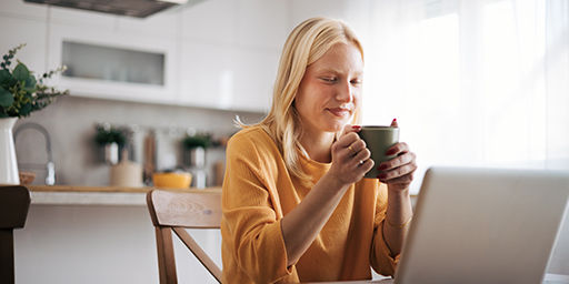 woman is holding a mug and watching something on her computer