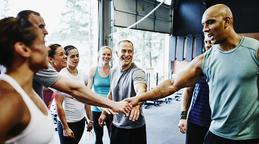 Laughing group of diverse friends celebrating together in huddle at the end of workout in gym