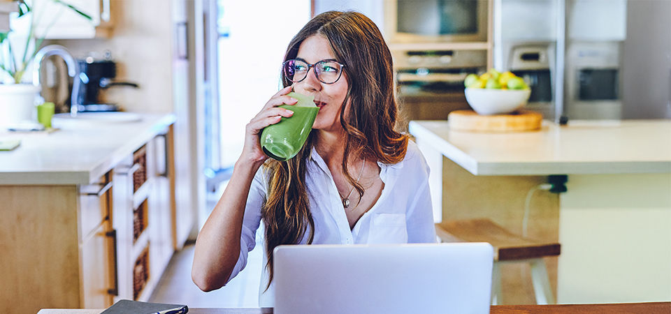 female at computer drinking green juice