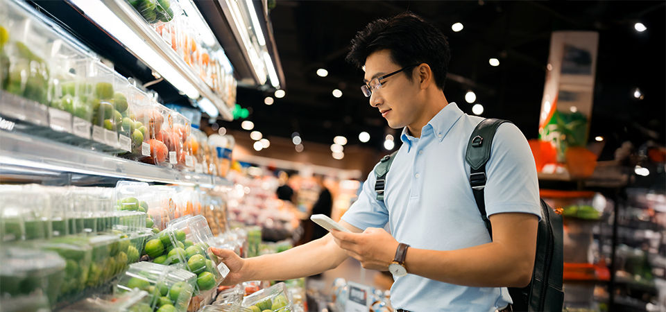 Young Asian man using smart phone  and choosing fresh organic fruits in supermarket.