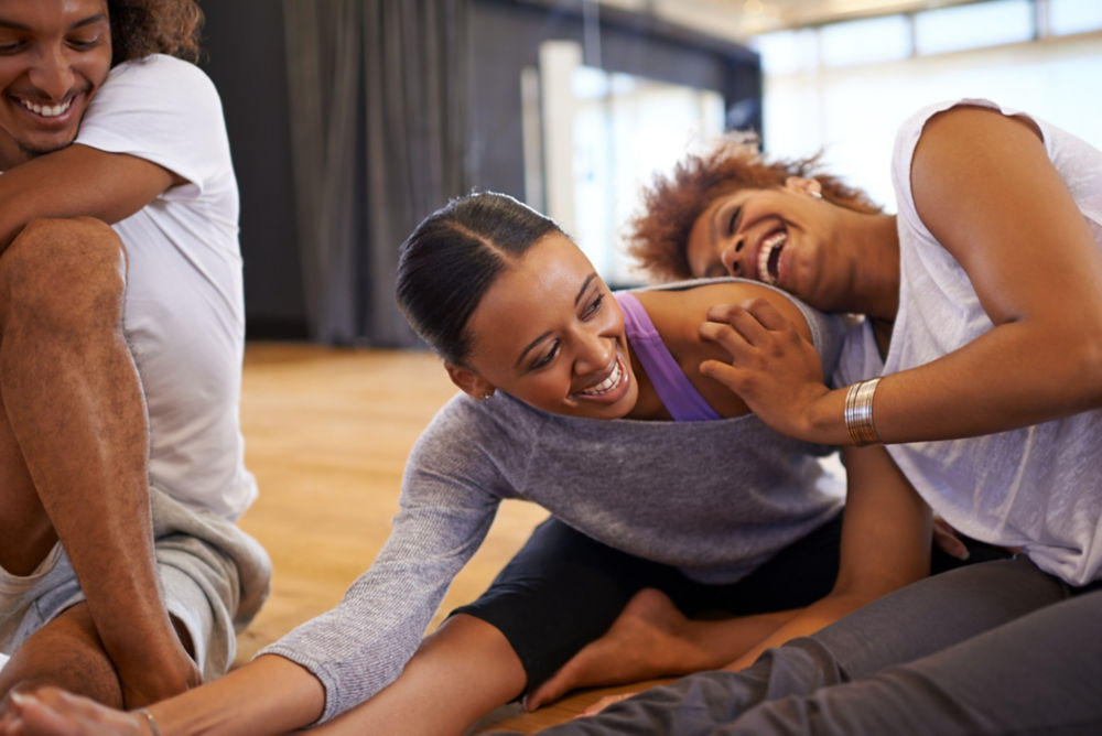 Fotografía de tres jóvenes bailarinas felices elongando en el piso