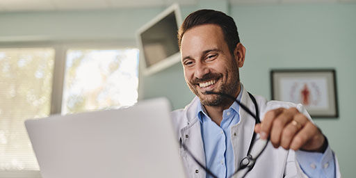 Happy male doctor surfing the Internet on a computer in the office at hospital.