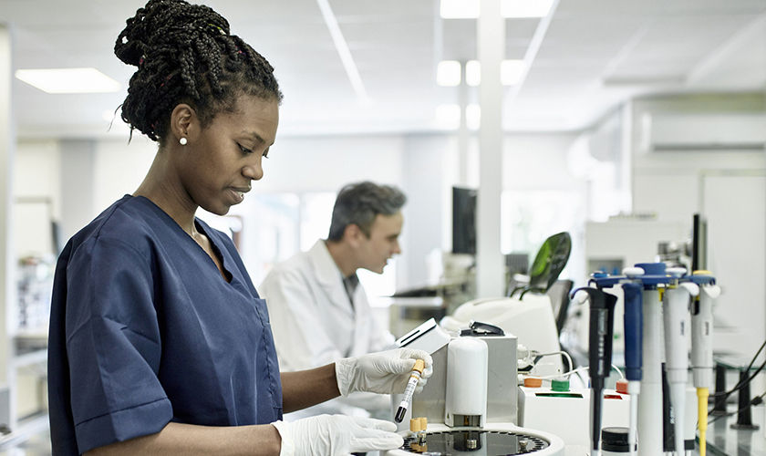 Smiling African female pathology technician in blue scrubs preparing test tubes for analysis in Buenos Aires clinical analysis laboratory.