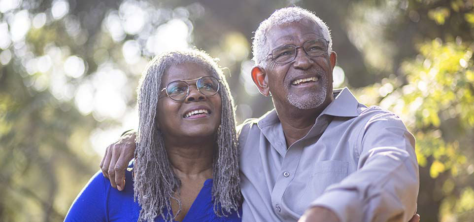 Una pareja de adultos mayores sonríe y reflexiona al aire libre