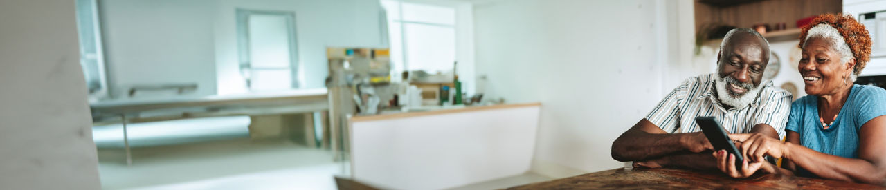 Pareja de adultos mayores utilizando un teléfono inteligente en la cocina en casa.