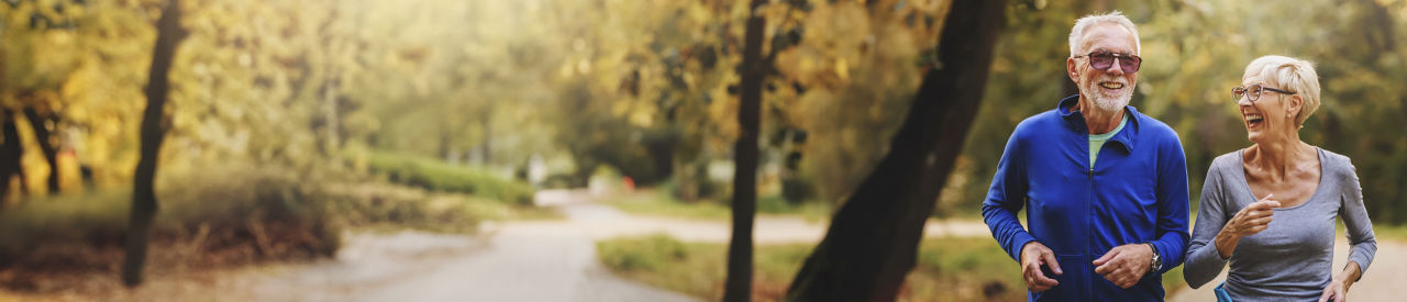 Pareja de adultos mayores feliz haciendo jogging al aire libre en un día de otoño.