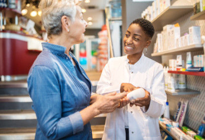 Joven farmacéutico sonriendo y ayudando a una mujer mayor con el medicamento