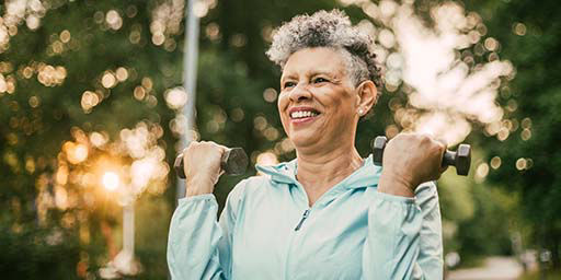 senior outside smiling and holding weights 